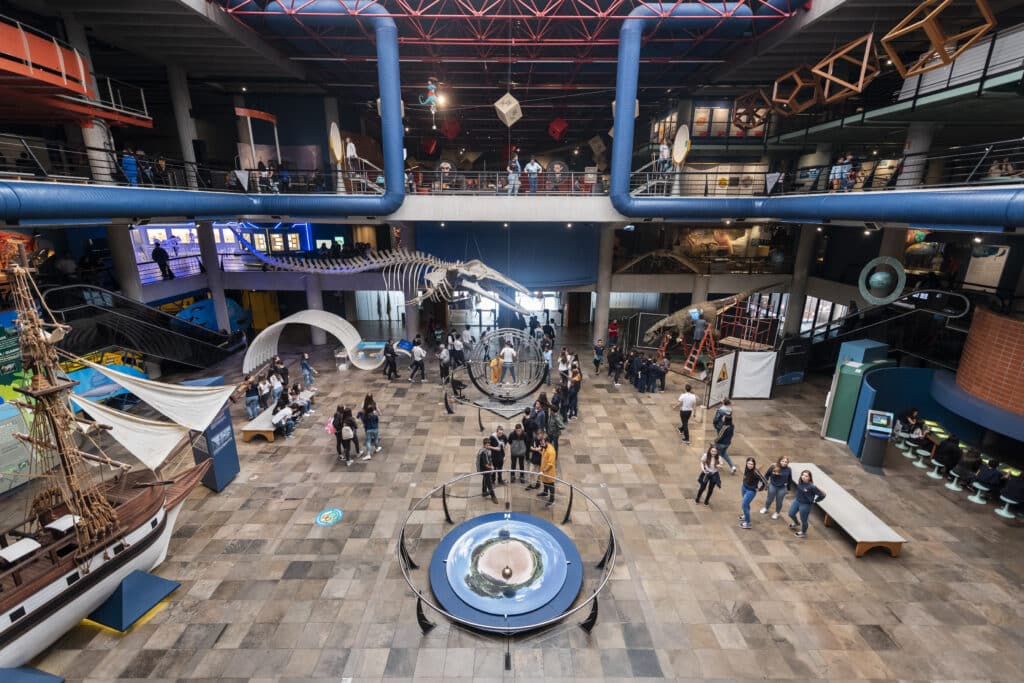 Parte interna do Museu de Ciência e Tecnologia, com exposições interativas e várias pessoas andando. Imagem para ilustrar post sobre o que fazer em Porto Alegre.