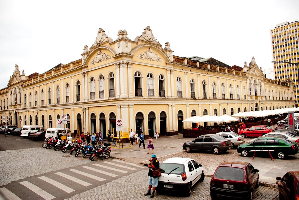 Frente do Mercado Público, com carros e motos estacionados, e barracas na lateral. Imagem para ilustrar post sobre o que fazer em Porto Alegre.