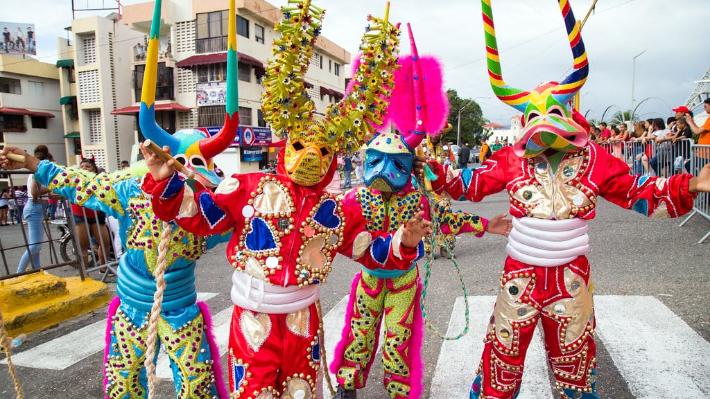 Quatro pessoas em trajes coloridos, máscaras vibrantes e chifres grandes e ornamentados posam energicamente em uma rua durante durante o Carnaval em Santiago.