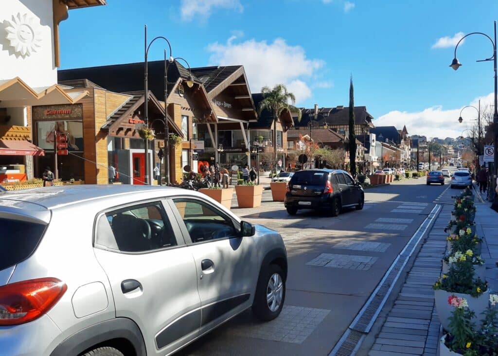carros passando na avenida borges de medeiros, em gramado, mostrando diversas construções em estilo europeu ladeando a avenida.