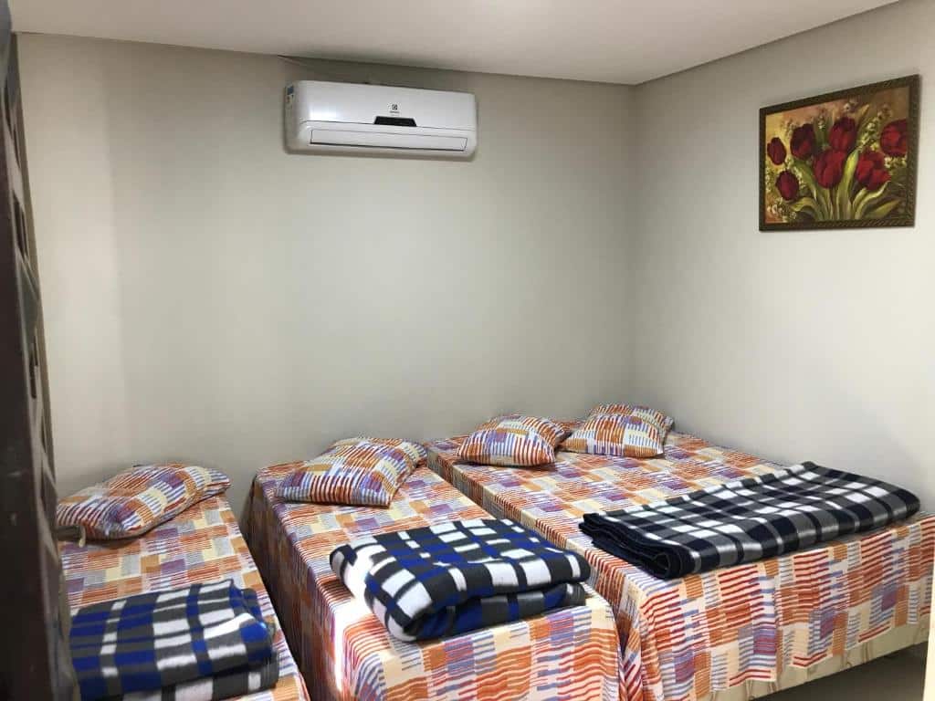 Três camas de solteiro na Pousada Santa Maria com roupas de cama estampadas e cobertores dobrados em um quarto simples com ar-condicionado e pintura de tulipas na parede.