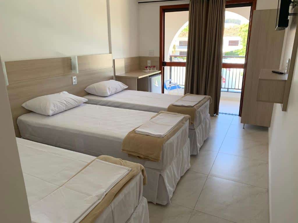 Um quarto da Pousada Santa Fé com três camas de solteiro, cada uma com lençóis brancos e mantas bege, de frente para uma janela com cortinas marrons.