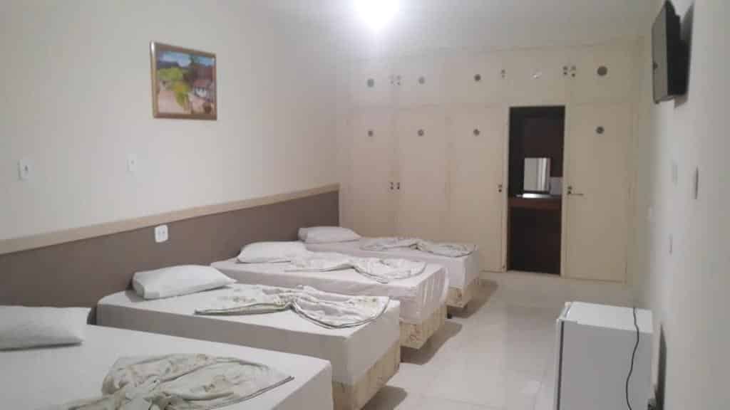 Um quarto da Pousada São Bento com quatro camas de solteiro, um frigobar, uma TV na parede e um quadro na parede.
