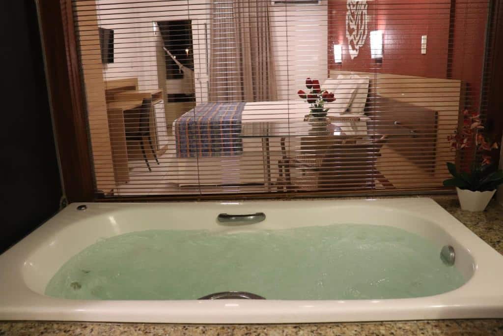Quarto do Hotel Pousada do Sol com hidro e janela com vista para o quarto de casal com TV e sacada com rede de descanso