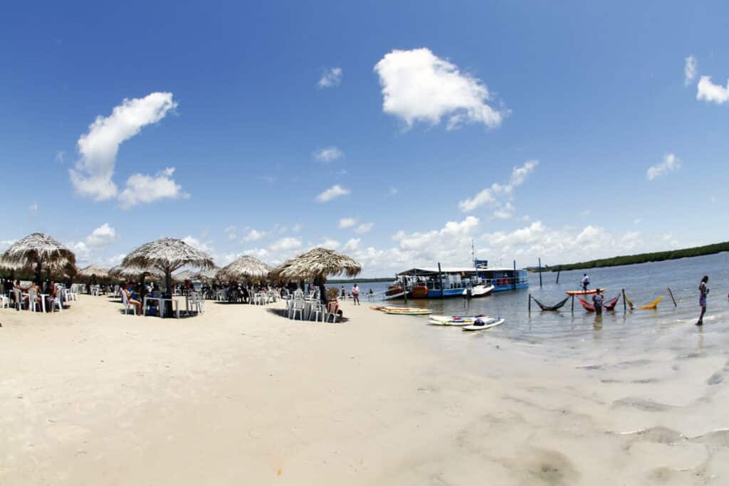 Crôa do Goré, em Aracaju, com guarda-sóis naturais, redes na água e um barco perto da orla