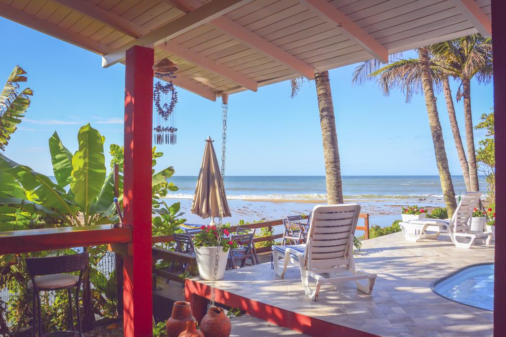 Varanda à beira-mar da Pousada Canto da Brava, em Balneário Camboriú, com uma piscina, espreguiçadeiras e mesas com cadeiras em volta e bem a frentem tem o mar com ondas pequenas, em um dia ensolarado e com poucas nuvens