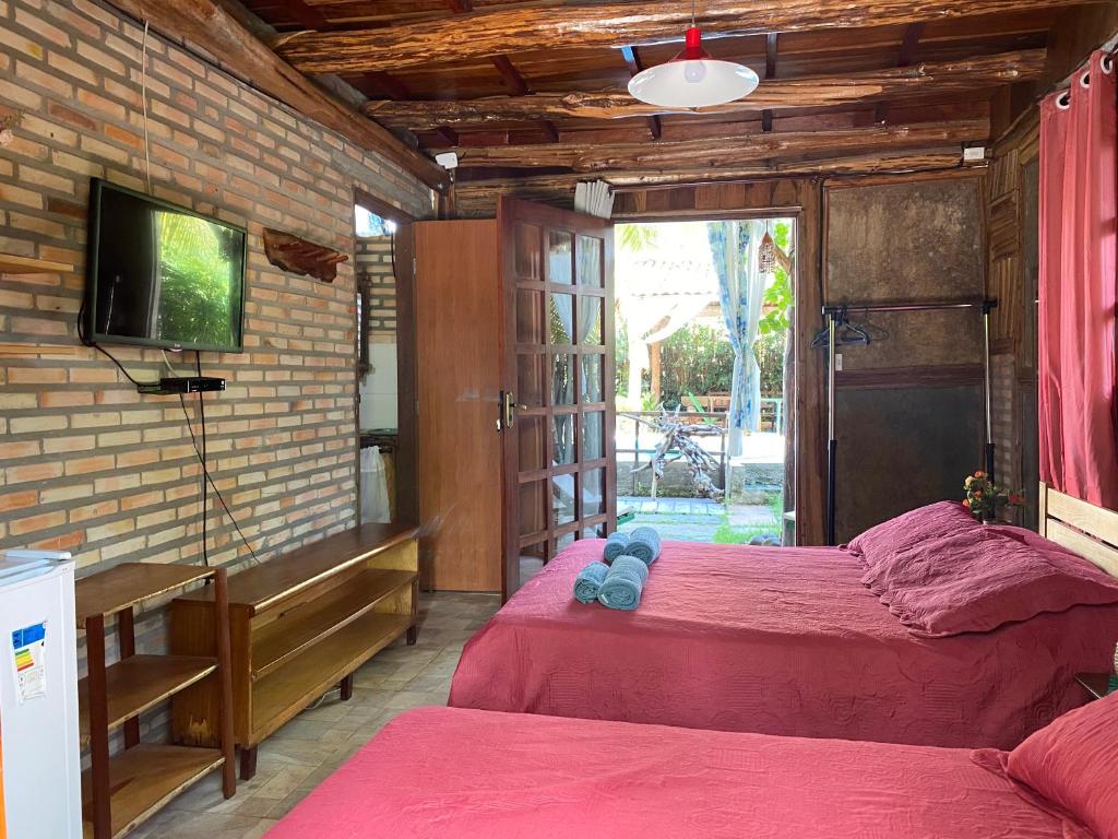 Quarto da Pousada Pedaço do Paraíso com paredes de tijolos com duas camas, TV, frigobar, porta aberta para um jardim e entrada de luz natural. Representa o post de pousadas em Barra Grande no Piauí.