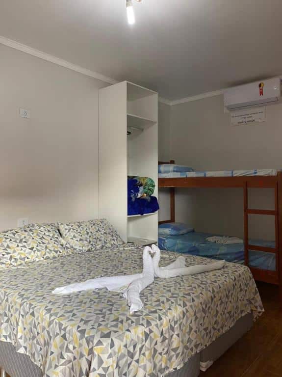 Quarto da Pousada Papaya com uma cama de casal, um beliche, roupas de cama estampadas e toalhas dobradas em forma de cisne sobre a cama.