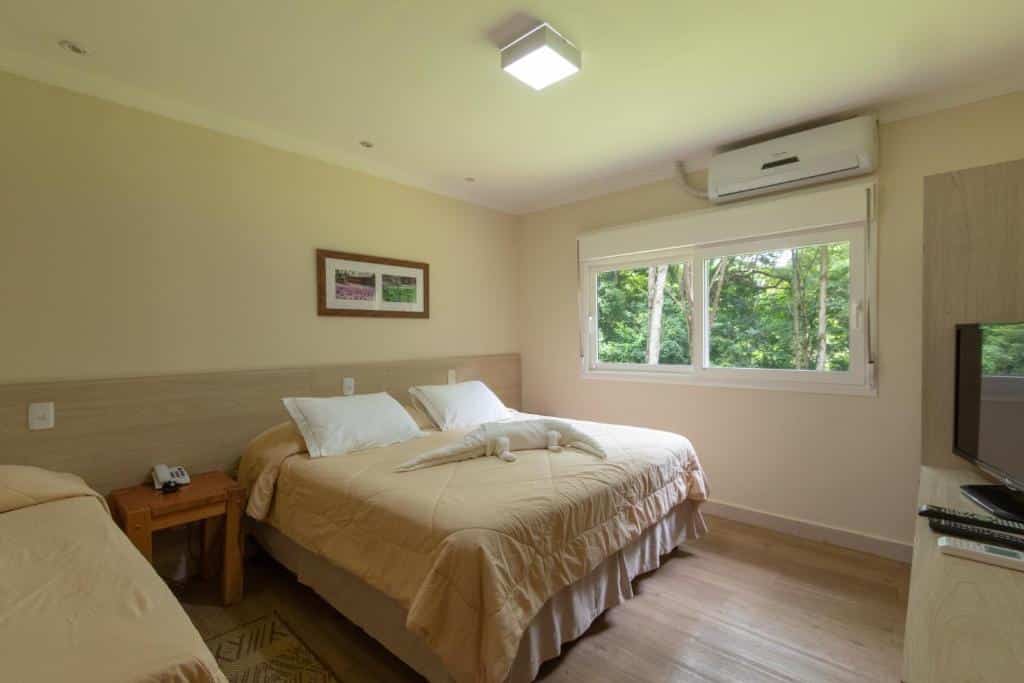 quarto da Pousada Olho D'Água com uma cama de casal e uma cama de solteiro, uma janela com vegetação e um ar-condicionado acima da janela.