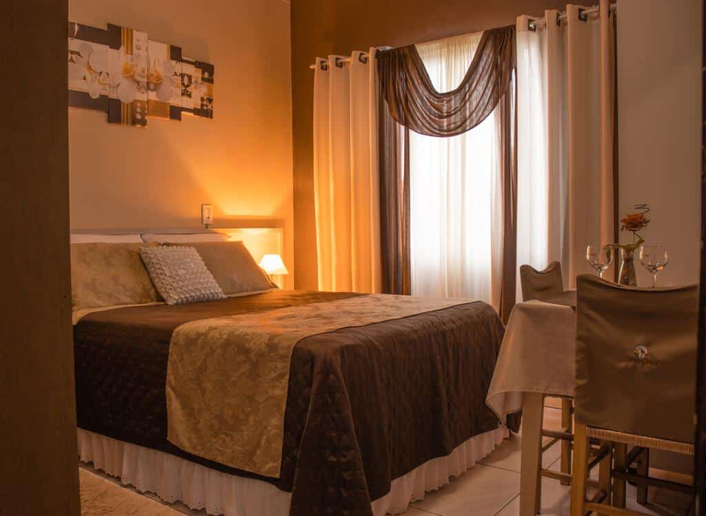 suíte da Pousada Serra Geral em Cambará do Sul mostrando uma cama de casal e uma pequena mesa de madeira quadrada com duas cadeiras e duas taças de vidro