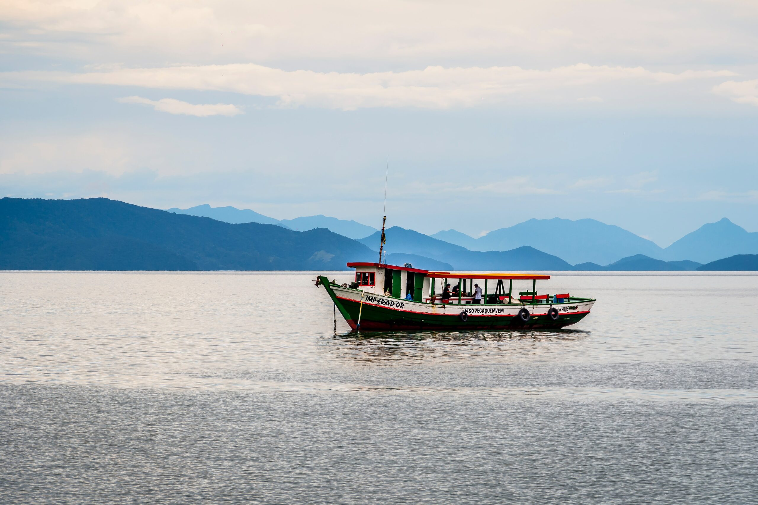Vista de um barco de pescadores em alto mar em São Sebastião, com montanhas ao fundo em dia claro.