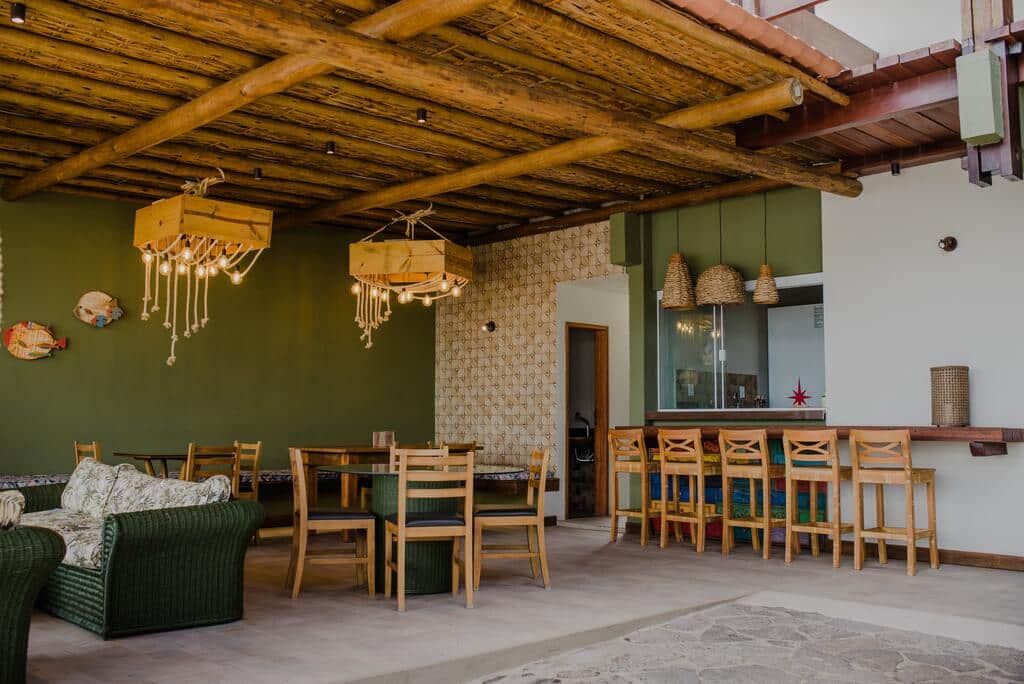 Área comum da pousada Pier do Pontal em Ilhéus, com banquetas, sofá, mesa com cadeiras e luminárias feitas com caixotes