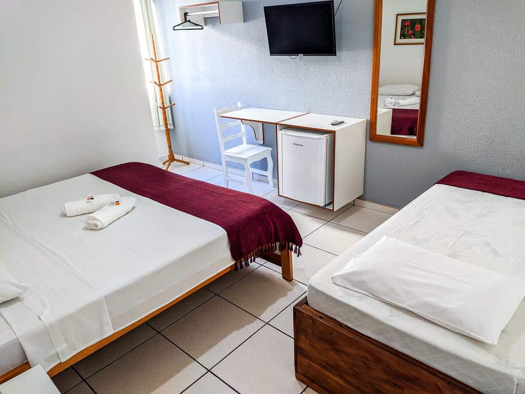 Pousada Bem Me Quer em Ilhéus com uma cama de casal, uma cama de solteiro, uma TV, um frigobar, um cabideiro e um espelho de corpo inteiro