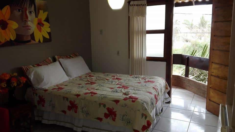 suíte da Pousada Casarão Praia Dourada com cama de casal, pintura de índio sobre a cabeceira e uma sacada 