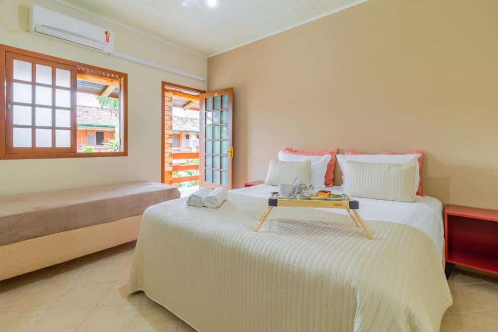 Um quarto com uma cama de casal, uma cama de solteiro, uma bandeja com toalhas e uma porta aberta que dá para uma área externa.