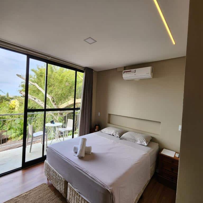 Quarto moderno com janela grande, cama de casal, ar-condicionado e varanda com mesa e cadeiras ao ar livre, na Casa Arrô - Pousada Boutique, para representar pousadas em Itajaí.