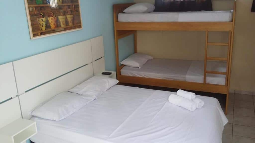 Um quarto da Pousada d'Ibiza com uma cama de casal e um beliche, todos com roupa de cama e toalhas brancas, ao lado de piso de azulejos e paredes claras.