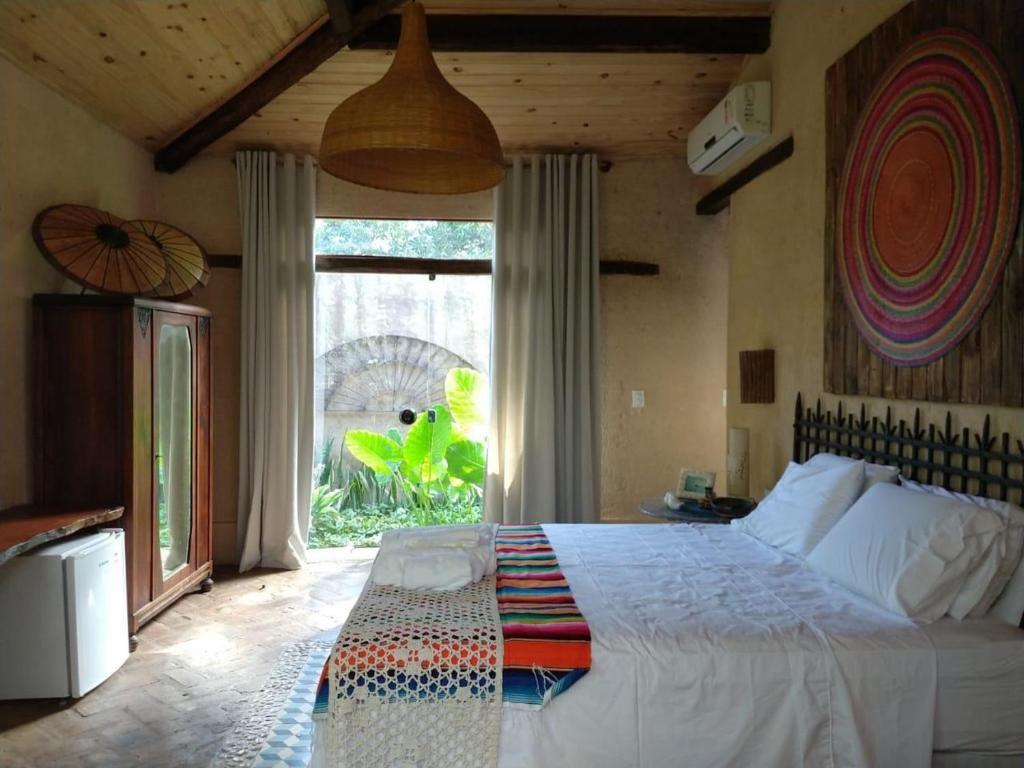 Um quarto aconchegante no Zazen Pousada by Santoregano na Praia da Garça Torta, com uma cama de casal, teto de madeira, janela grande e decoração colorida, com vista para um jardim, para representar pousadas em Maceió.