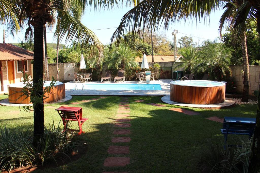 Um quintal com piscina da Monte Carlo Pousada, duas banheiras de hidromassagem redondas, palmeiras e mesas no pátio com guarda-sóis.