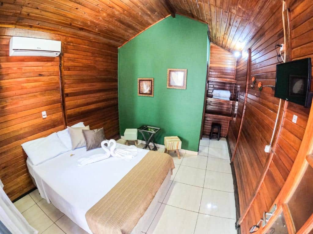 Um quarto da Pousada dos Chalés, uma das pousadas em Olímpia, com painéis de madeira, uma cama de casal, parede verde, TV, ar-condicionado e quadros emoldurados.