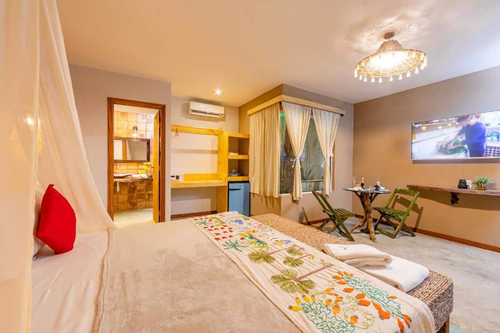 Quarto da pousada Vila Parnaíba com uma cama, mesa pequena com cadeiras, TV na parede e vista para o banheiro.