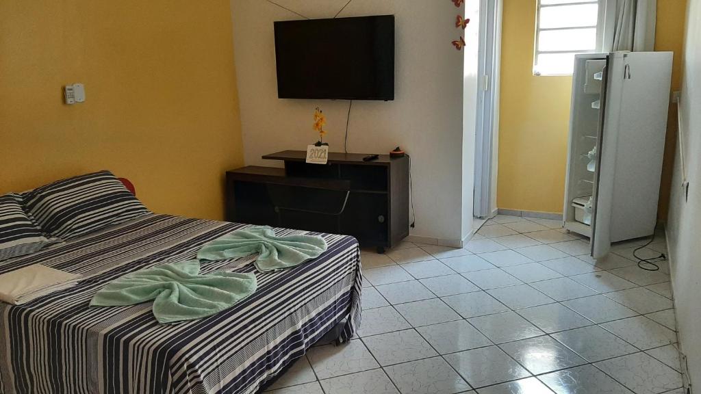 Quarto da Pousadas Portal das Araras com uma cama listrada, TV na parede, armário, frigobar e piso de azulejos com paredes amarelas e brancas.