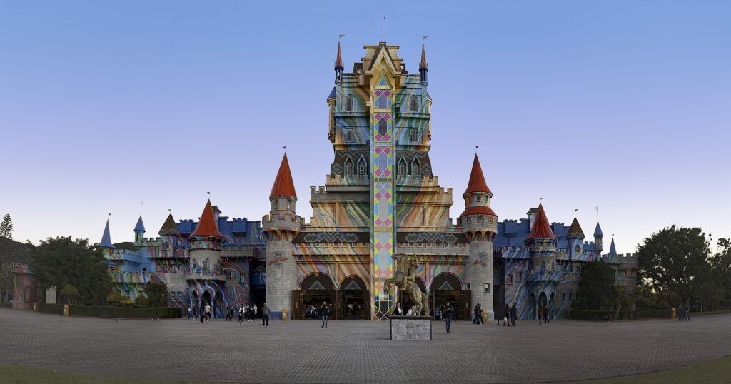 Castelo colorido do Beto Carrero World, em estilo de conto de fadas, com várias torres e uma coluna alta e padronizada na frente, visto ao pôr do sol.