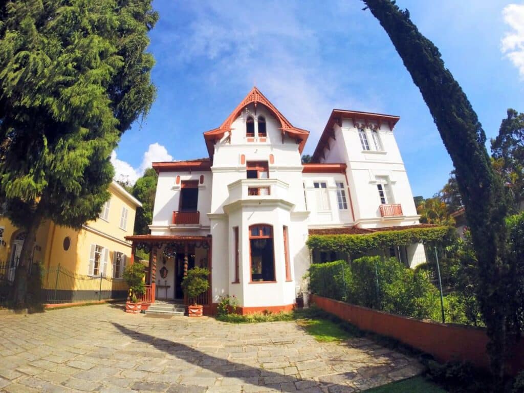 Faixada da Pousada Imperial Koeler, faixada branca com janelas cercado por um jardim. 