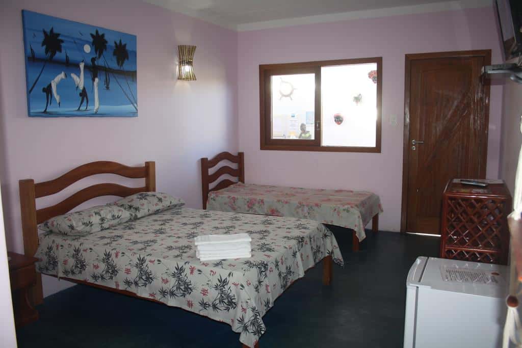 Um quarto da Villa Tropicale com duas camas, colchas florais, uma janela, uma porta, arte na parede, um frigobar e toalhas em uma cama.