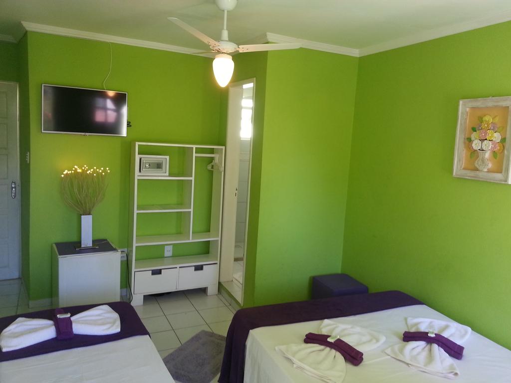 Um quarto do Hotel Pousada Papaya Verde com paredes verdes, duas camas, uma TV, ventilador de teto, estante e uma porta para o banheiro.