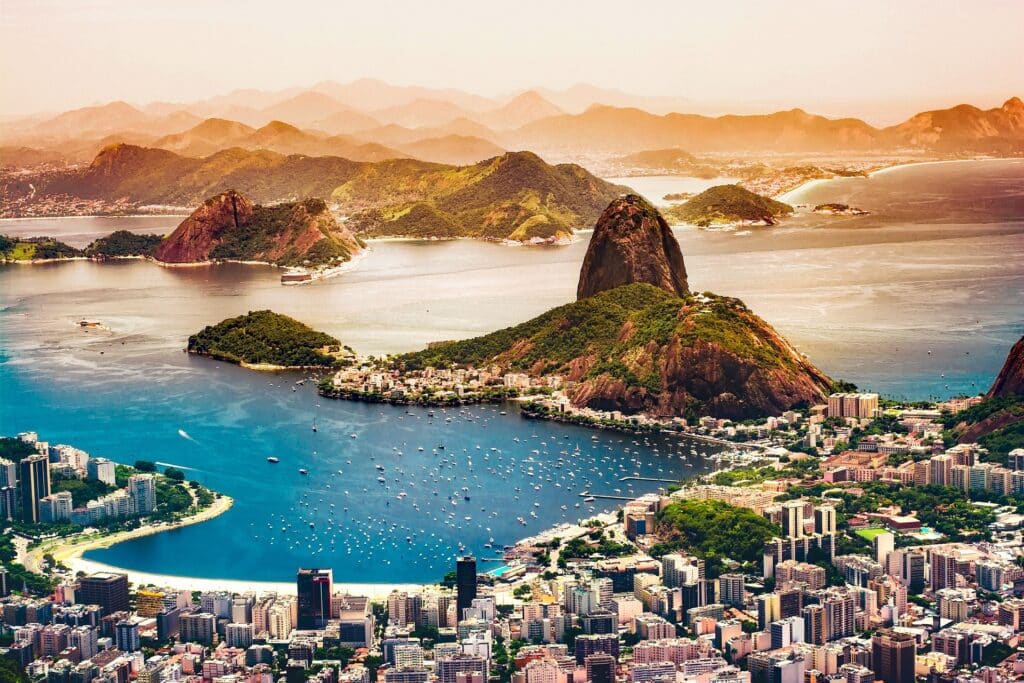 Vista aérea do Rio de Janeiro mostrando o Pão de Açúcar, os prédios da cidade, as praias e a baía ao redor.