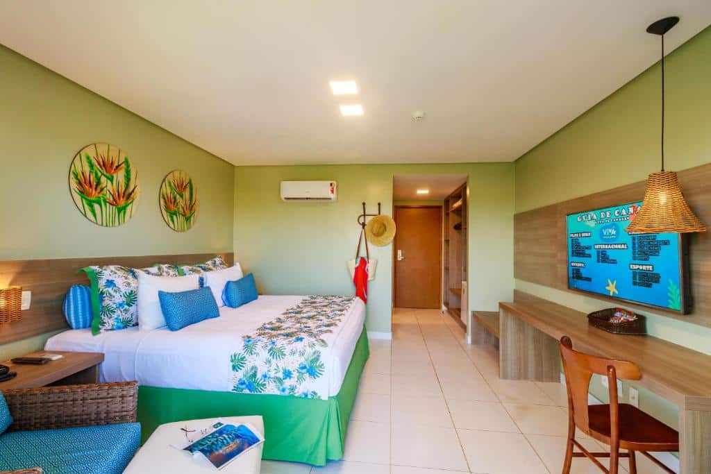 Quarto do Vivá Porto de Galinhas, um dos resorts para o Réveillon, com uma cama grande, decoração tropical, uma escrivaninha, arte na parede e iluminação clara.