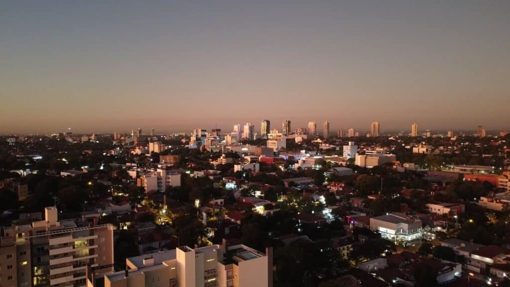 Cidade de Assunção no Paraguai, vista de cima durante a noite. Várias casas, prédios e construções, juntamente com algumas árvores. 