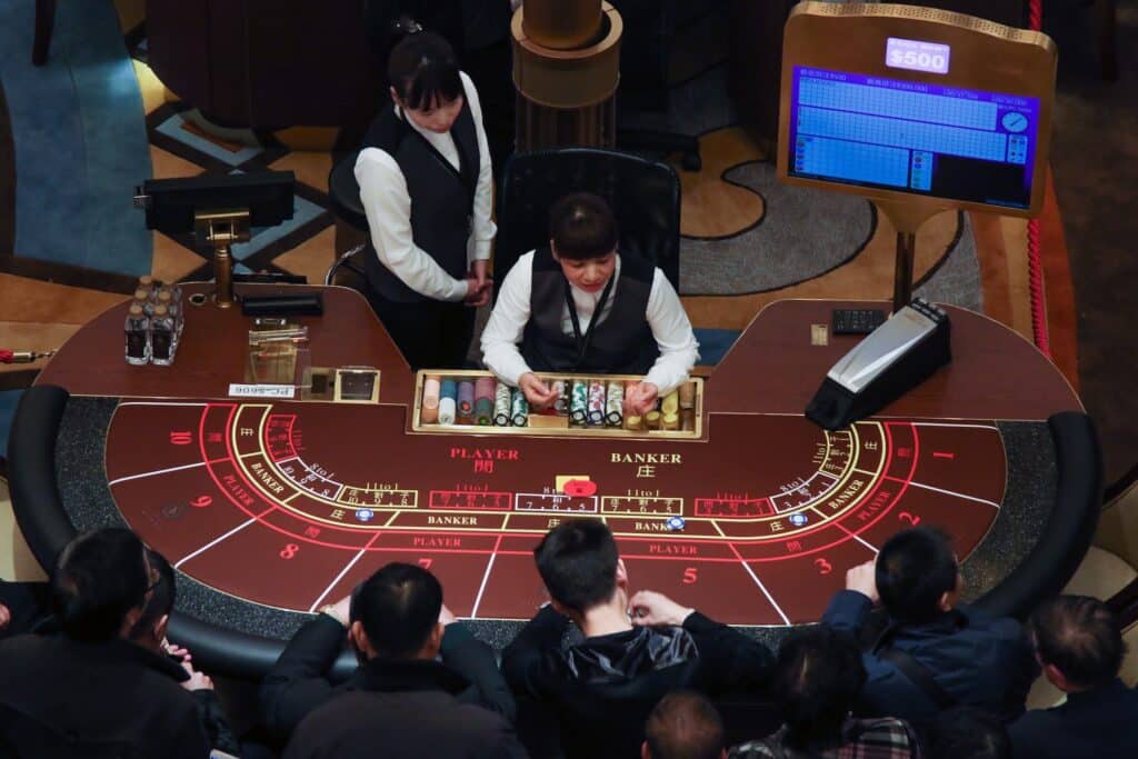 Mesa de jogo no cassino com quatro homens jogando e duas mulheres distribundo as peças. - Foto: Renato Marques via Unsplash